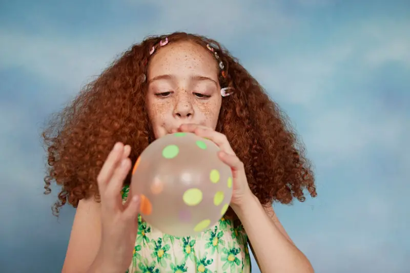 Niña inflando un globo con puntos pegados