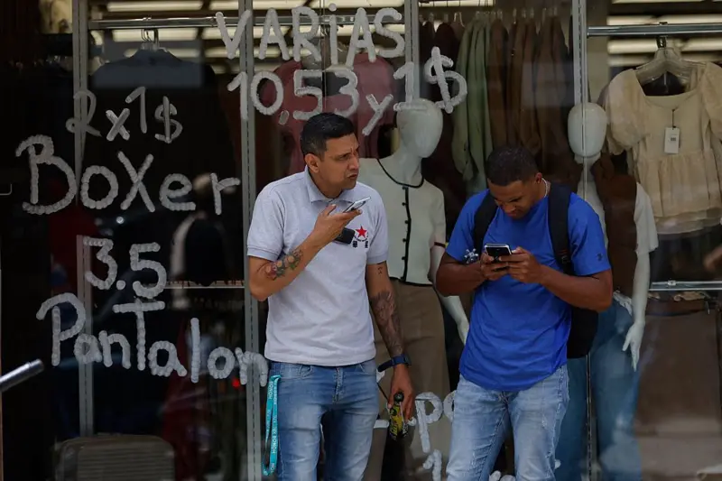 Personas frente a una tienda que exhibe precios en bolívares (moneda oficial venezolana) y dólares estadounidenses