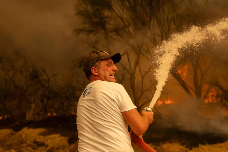 Un vecino lanzando agua con una manguera para apagar un incendio