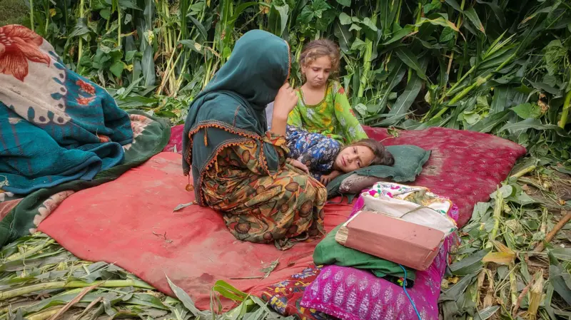 Una madre con la cabeza cubierta con un velo verde se refugia con dos niñas en una campo abierto