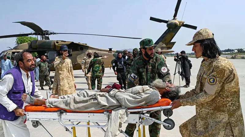 Voluntarios afganos y personal de seguridad talibán transportan a una víctima del terremoto evacuada por un helicóptero